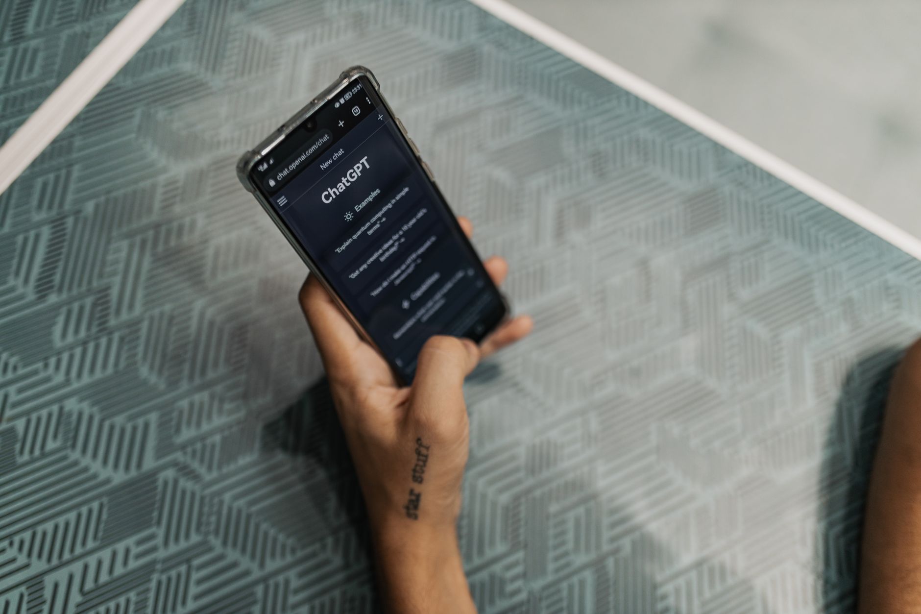 Primo piano di una persona che tiene uno smartphone con l'interfaccia di ChatGPT visualizzata su un tavolo a motivi