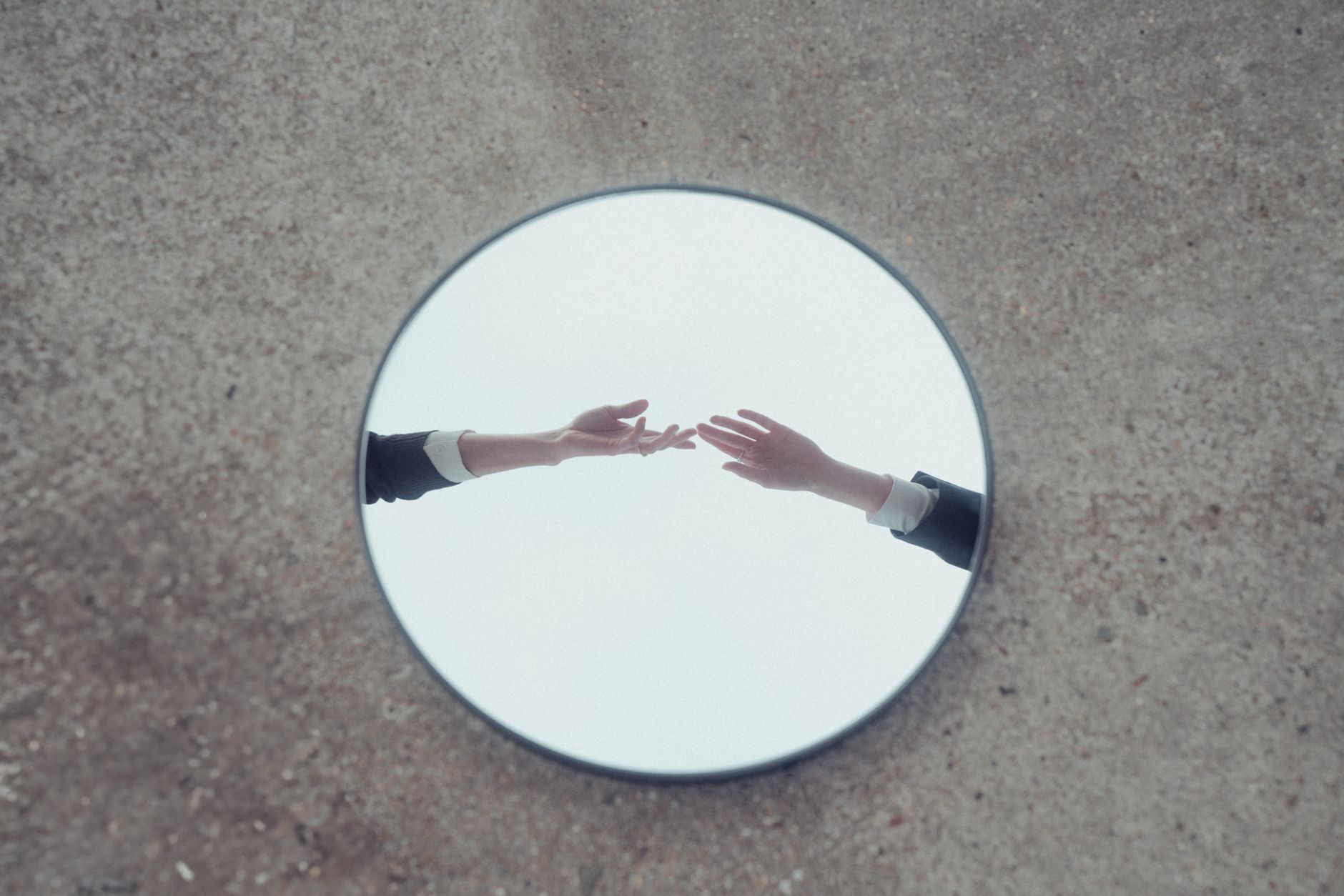 Conceptual image of hands reaching out, reflected in a round mirror on textured ground