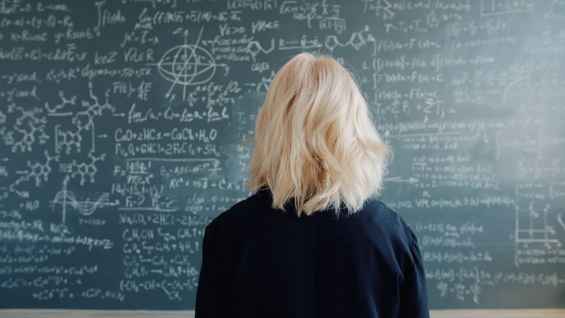 Rear view of a scientist studying equations on a blackboard, symbolizing innovation.