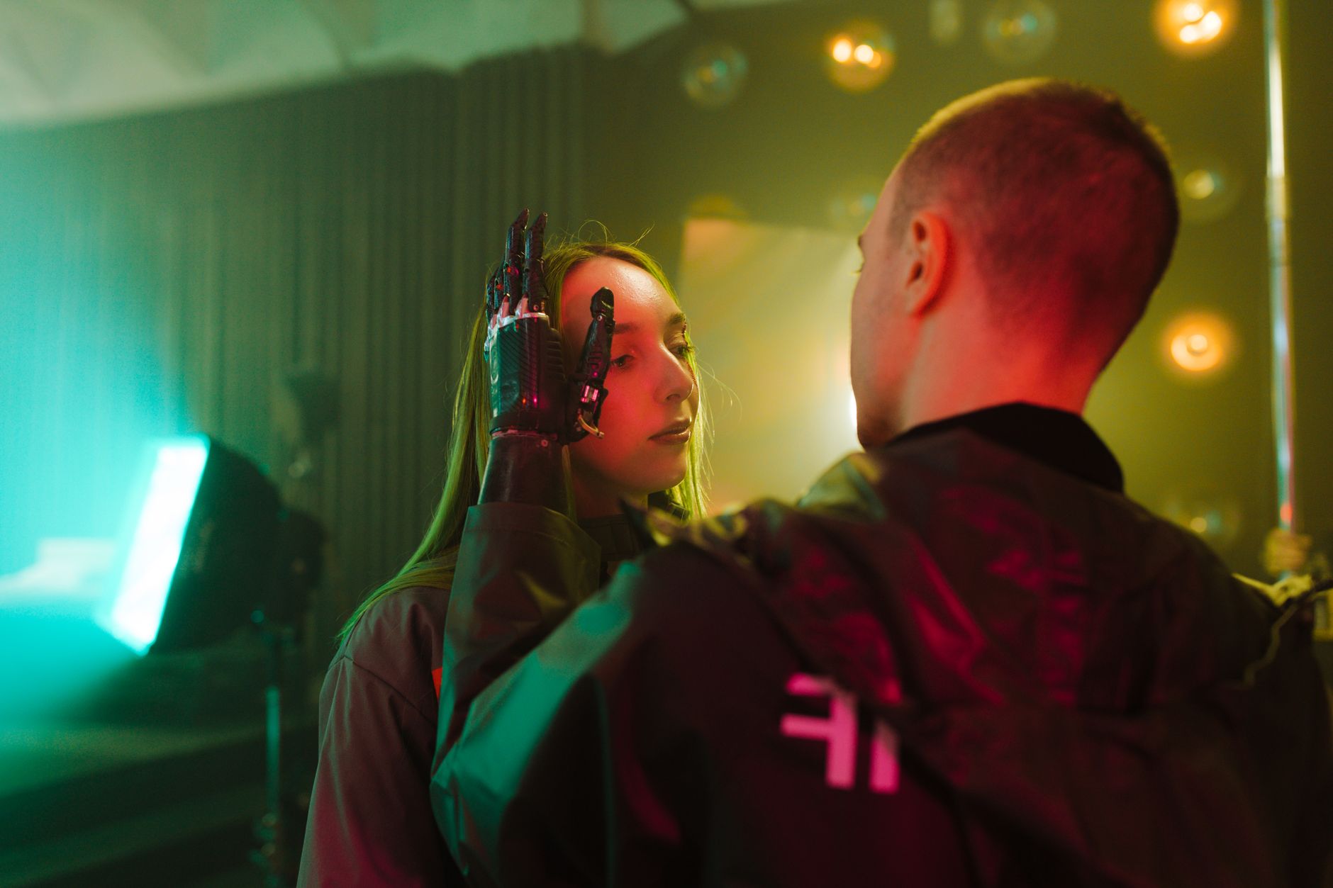 Un uomo con una mano protesica tocca delicatamente il viso di una donna in un'ambientazione cyberpunk