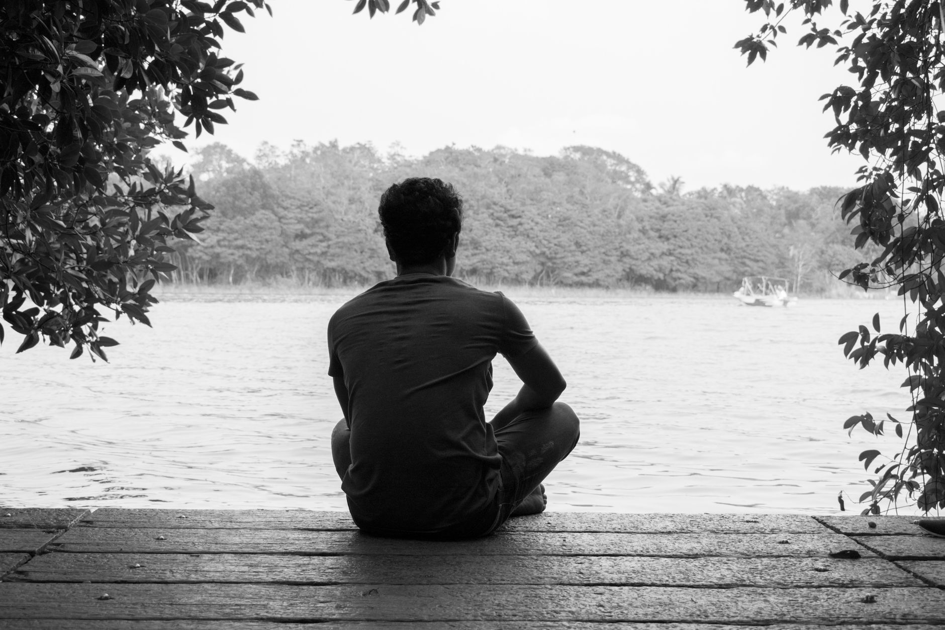 Una persona seduta contemplativa accanto a un lago, in bianco e nero, evoca la riflessione filosofica sulla natura del tempo e della coscienza